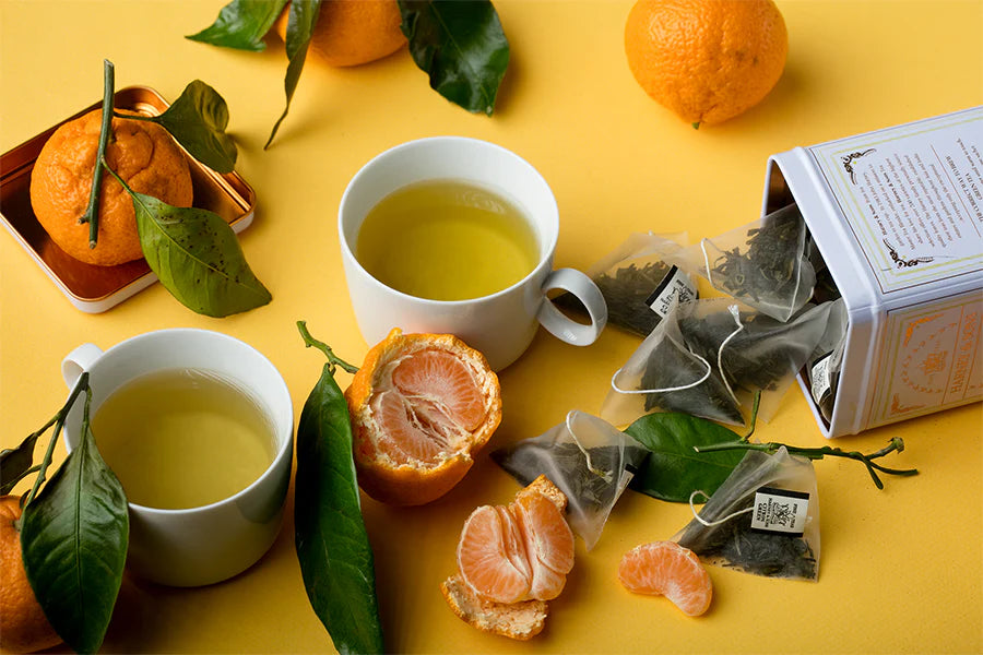 A cup of tea sits next to a box of tea bags A glass teapot filled with green tea next to two cups of tea